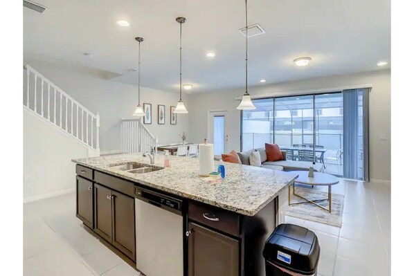 Enjoy a spacious living area with a sofa and coffee table, adjacent to a modern kitchen with a central island and large window offering a view of the outdoors.