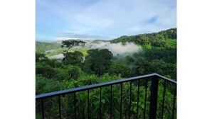 A lush green landscape with a clear sky and a view of a forested area from a balcony with a black railing. - Serene Jungle Stay with Breathtaking Views (San José province)