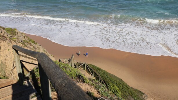 Une plage avec un escalier en bois descendant jusqu’au rivage, une plage de sable et l’océan.