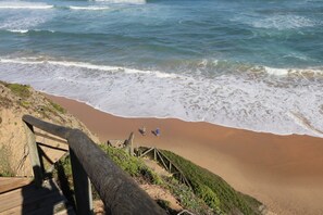 A beach with wooden stairs leading down to the shore, a sandy beach, and the ocean.