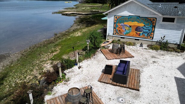 A lakeside property with a wooden deck, outdoor seating, and a mural on the side of a building. - Selkies Cave (Union)