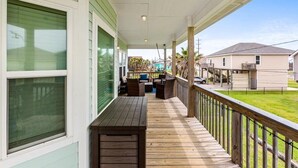 A covered porch with outdoor furniture, a wooden table, and a view of neighboring houses. - AJs Beach Haven - family fun- beautiful vacation home in Sea Isle (Galveston)