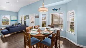 A dining area with a round table set for six, surrounded by wooden chairs with blue cushions. - AJs Beach Haven - family fun- beautiful vacation home in Sea Isle (Galveston)