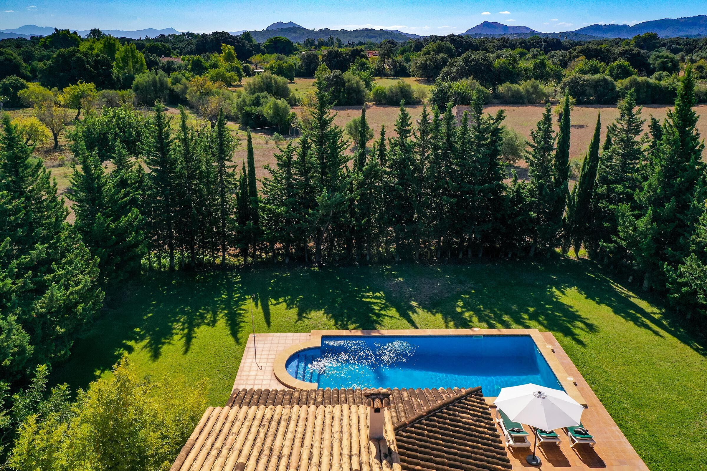 A pool with a wooden deck and lounge chairs, surrounded by trees and a view of distant hills.