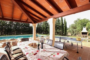Eine Terrasse im Freien mit Essplatz, Blick auf einen Swimmingpool und einen Grillbereich.