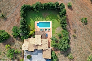 Eine Luftaufnahme eines Grundstücks mit Swimmingpool, einer Terrasse mit Liegestühlen und einem Gebäude mit Holzdach.