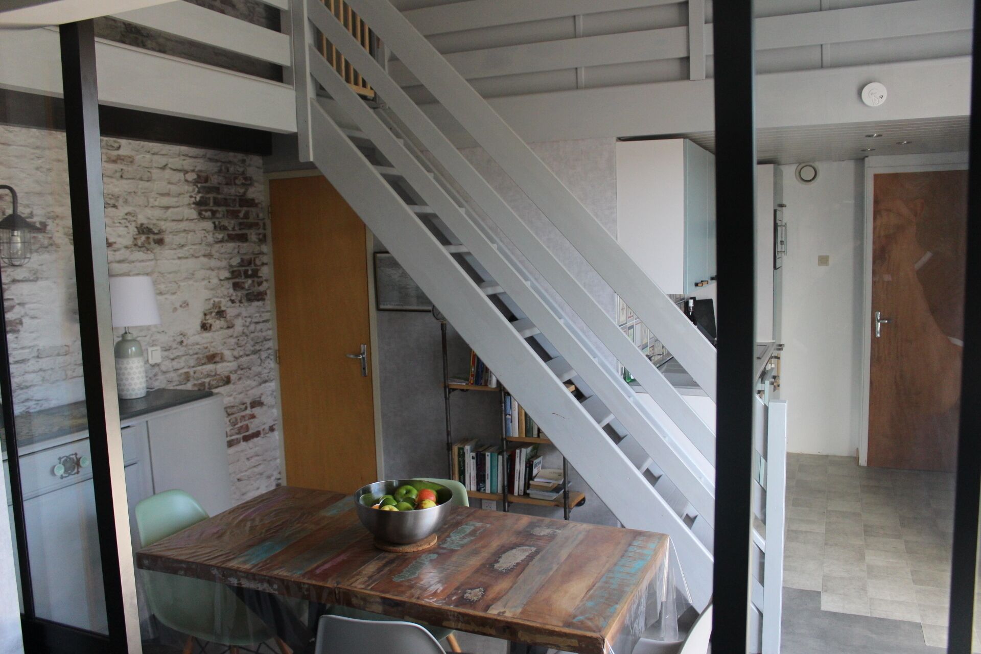 A dining area with a wooden table, a bowl of fruit, and a staircase leading to another level.