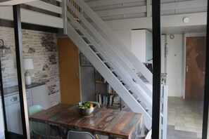Un coin repas avec une table en bois, un saladier rempli de fruits et un escalier menant à un autre niveau.