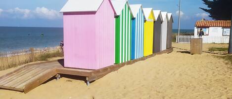 Een rij kleurrijke strandhutten met een houten terras ervoor.