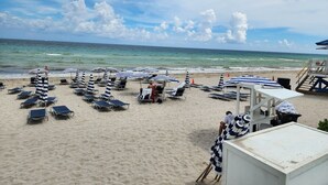 Une plage bordée de rangées de chaises longues et de parasols rayés, avec une tour de surveillance et l’océan en toile de fond.