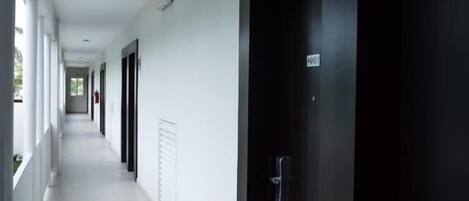 A long, narrow hallway with white walls and black doors, leading to a dark door at the end.