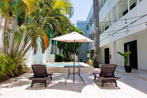 Un área junto a la piscina con dos sillas de mimbre, una mesa y una sombrilla.