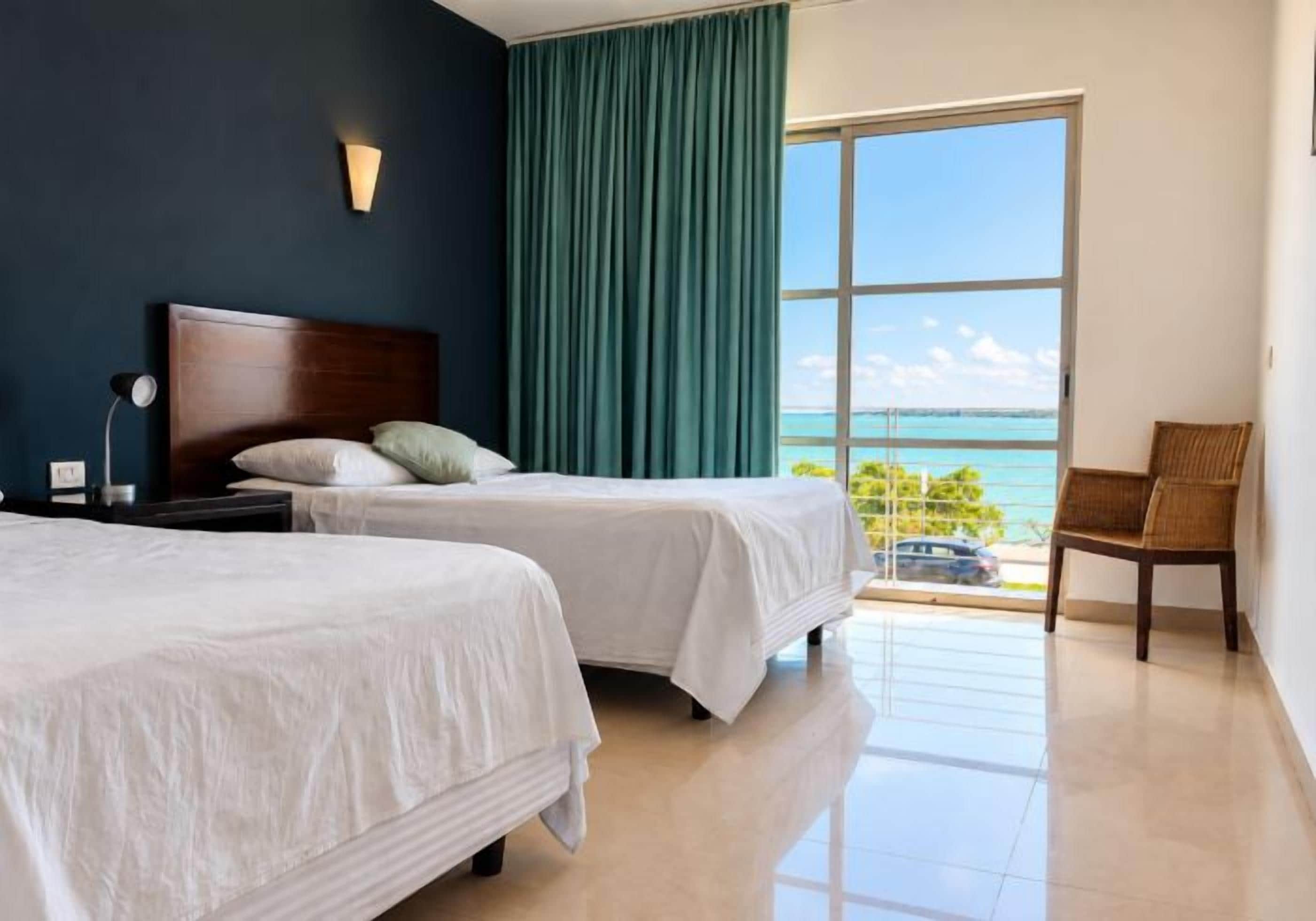 Habitación de hotel con dos camas, una mesita de noche, una silla y vista al océano.