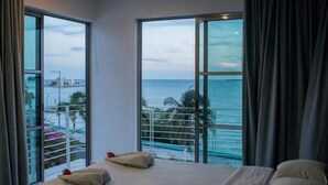 A hotel room with a large bed, two windows offering a view of the sea and a distant cityscape. - Hotel Noor (Chetumal)