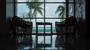 A room with a large window offering a view of the beach and palm trees. - Hotel Noor (Chetumal)