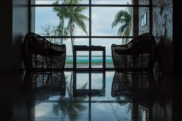 A room with a large window offering a view of the beach and palm trees. - Hotel Noor (Chetumal)
