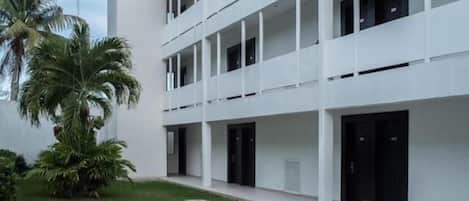 A modern building with a pool, white exterior, and multiple balconies.