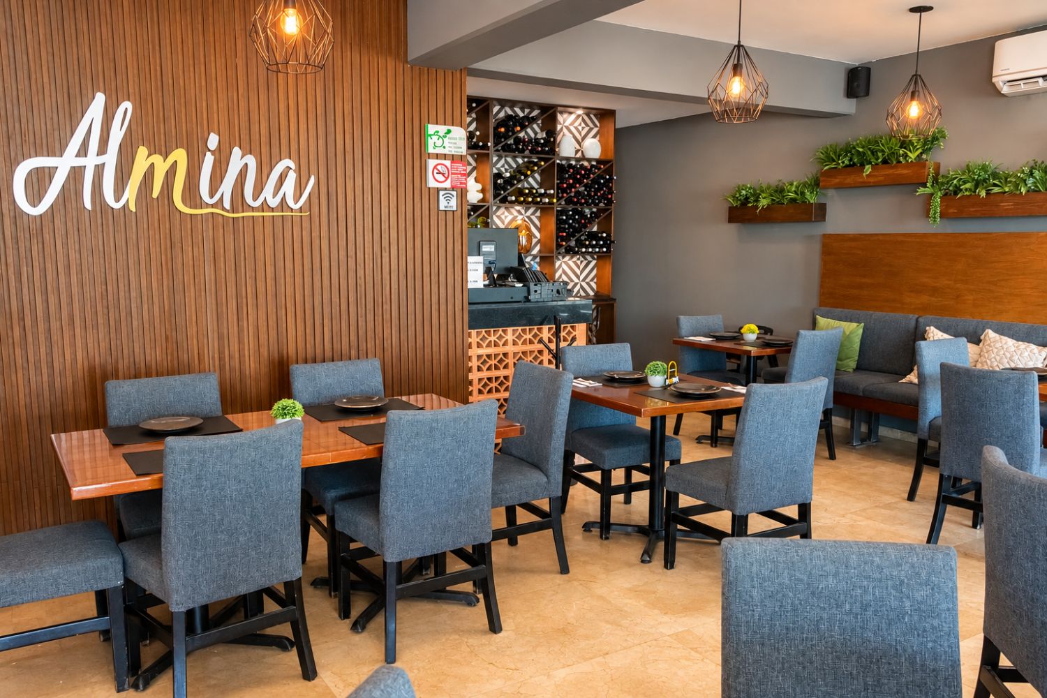 L’intérieur d’un restaurant présente un mur en bois, une enseigne indiquant « Almina » et un coin bar avec un mur orné de motifs.