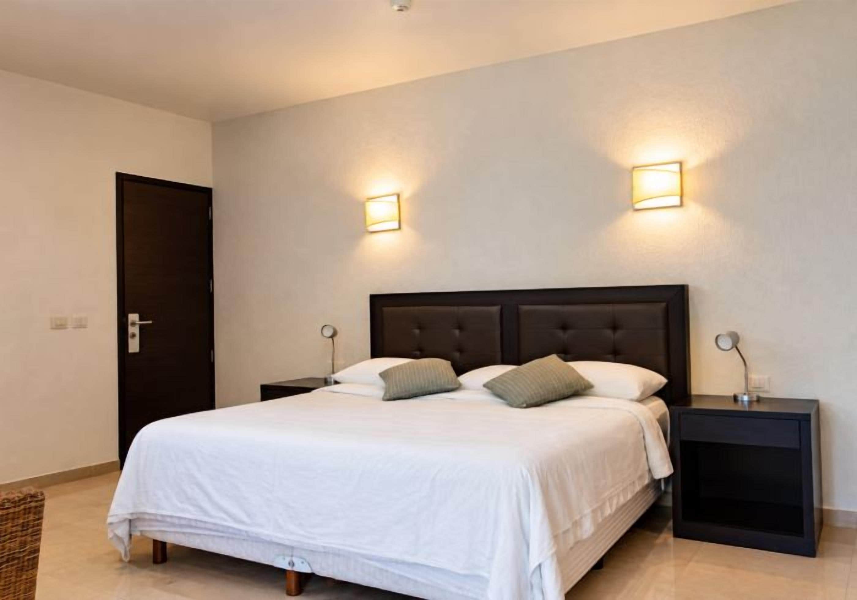 Habitación de hotel con cama, dos mesitas de noche y dos luces fijadas a la pared.