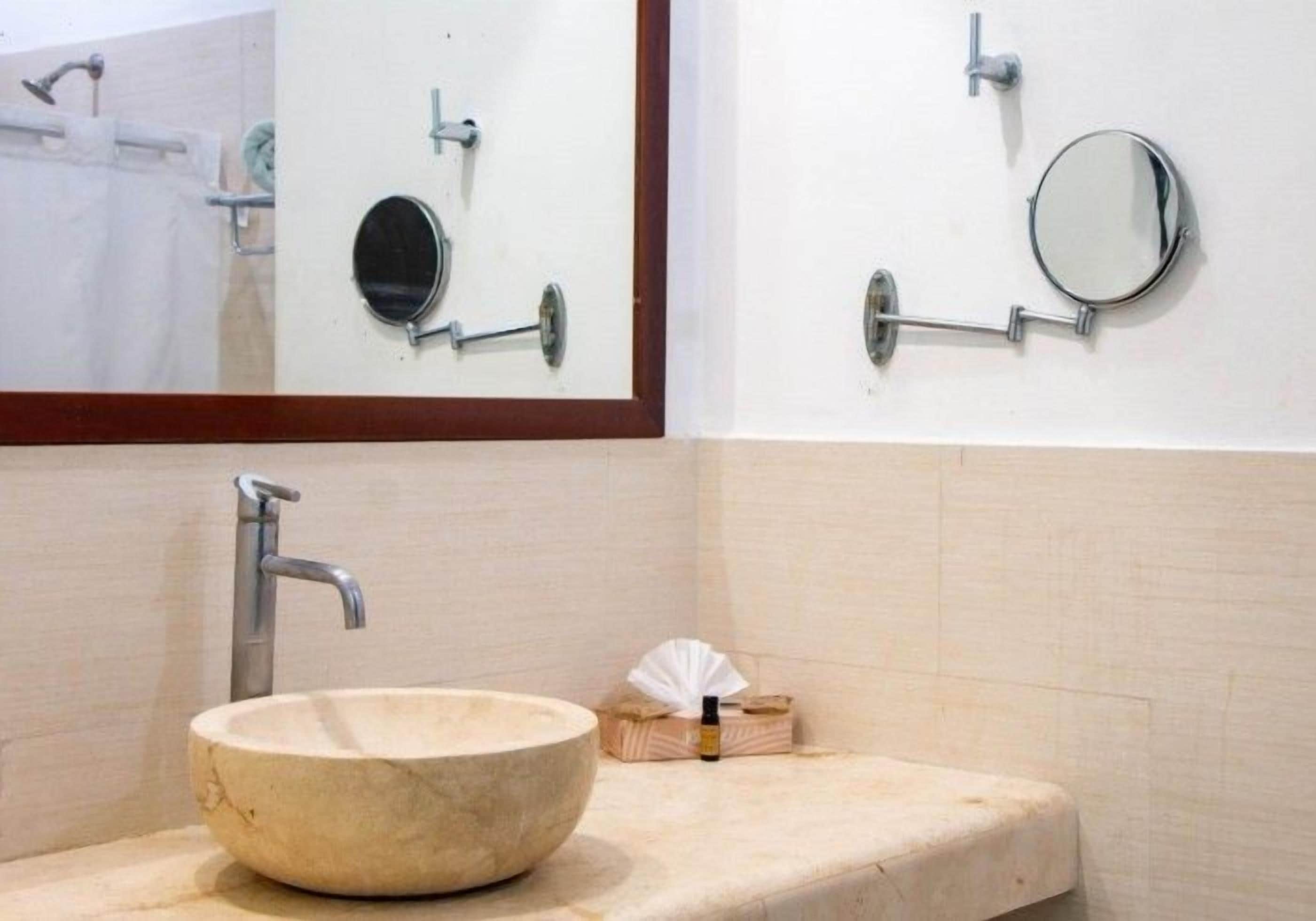 A bathroom with a round marble sink, a mirror, and a towel dispenser.
