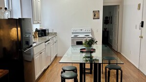 A modern kitchen with white cabinets, a black refrigerator, a stove, and a glass dining table with four stools.