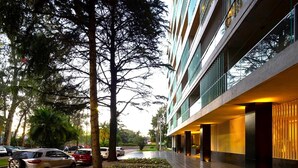 A modern building with a covered walkway, parked cars, and trees. - Stylish apartment by river with pool & grill (Olivos)