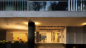 A modern building entrance with a concrete facade, a large pillar, and a set of stairs leading to an interior space. - Stylish apartment by river with pool & grill (Olivos)