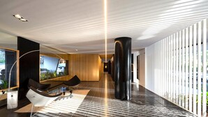 A modern hotel lobby with a long corridor, a large black pillar, and a seating area with chairs and a table. - Stylish apartment by river with pool & grill (Olivos)