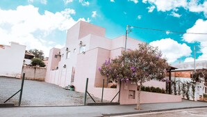 A modern building with a pink facade, a small tree with purple flowers, and a clear blue sky. - Pousada Shalom Capitólio (Capitólio)