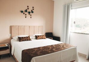 A hotel room with a large bed, a nightstand, a desk, and a view of the outdoors through a window. - Pousada Shalom Capitólio (Capitólio)