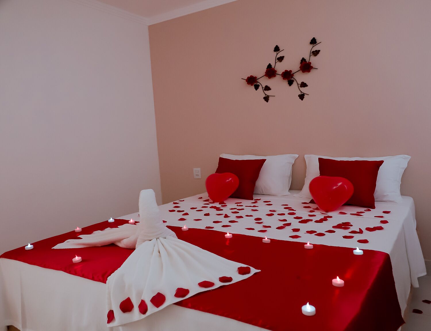 Een bed met rode en witte beddengoed, hartvormige kussens en een bloemenboeket.