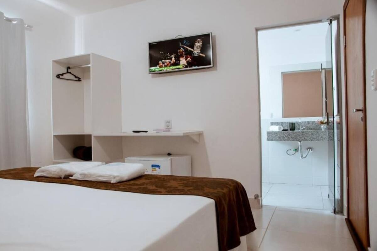 Hotellihuone, jossa on sänky, seinälle asennettu televisio, vaatekaappi ja kylpyhuone, joka näkyy avoimesta ovesta.