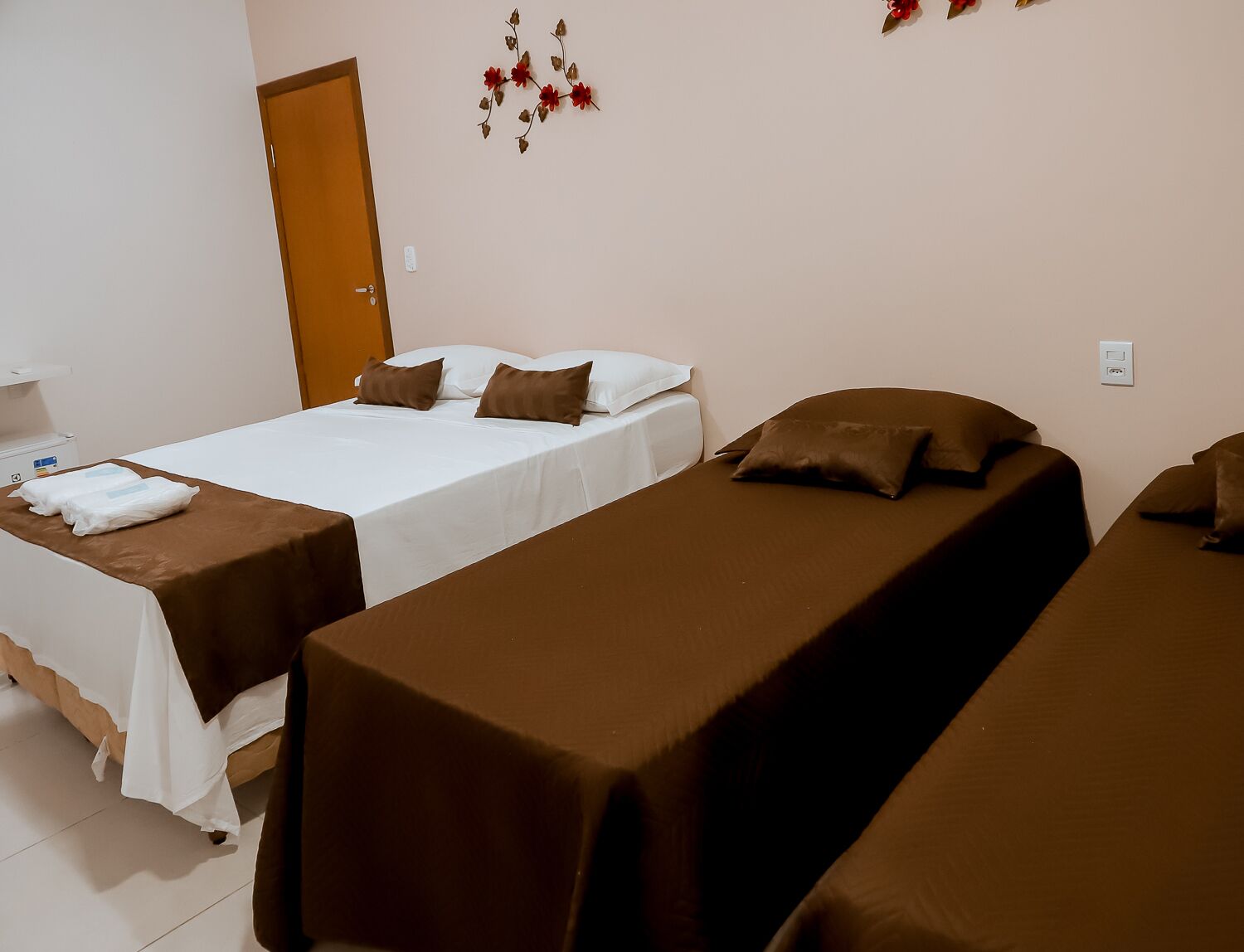 A hotel room with two beds, each with brown and white bedding, a wooden door, and a wall decoration.