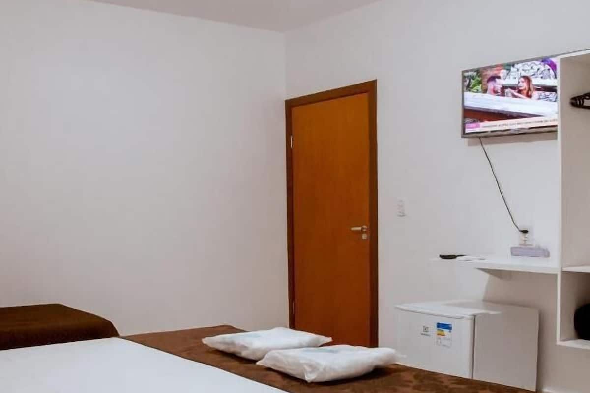 Hotellihuone, jossa on sänky, puuovi, televisio ja pieni valkoinen kaappi.