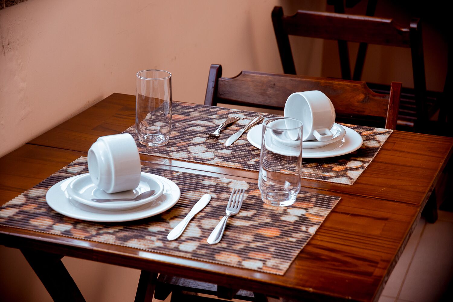 A dining table set with white plates, bowls, cutlery, and glasses, with a patterned placemat.