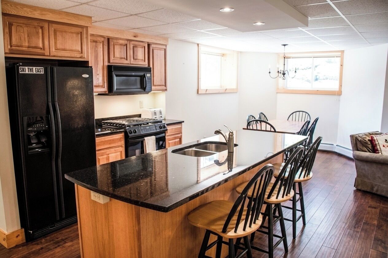 Une cuisine avec des meubles en bois, un réfrigérateur noir, un four à micro-ondes, une cuisinière et un coin bar avec des chaises.