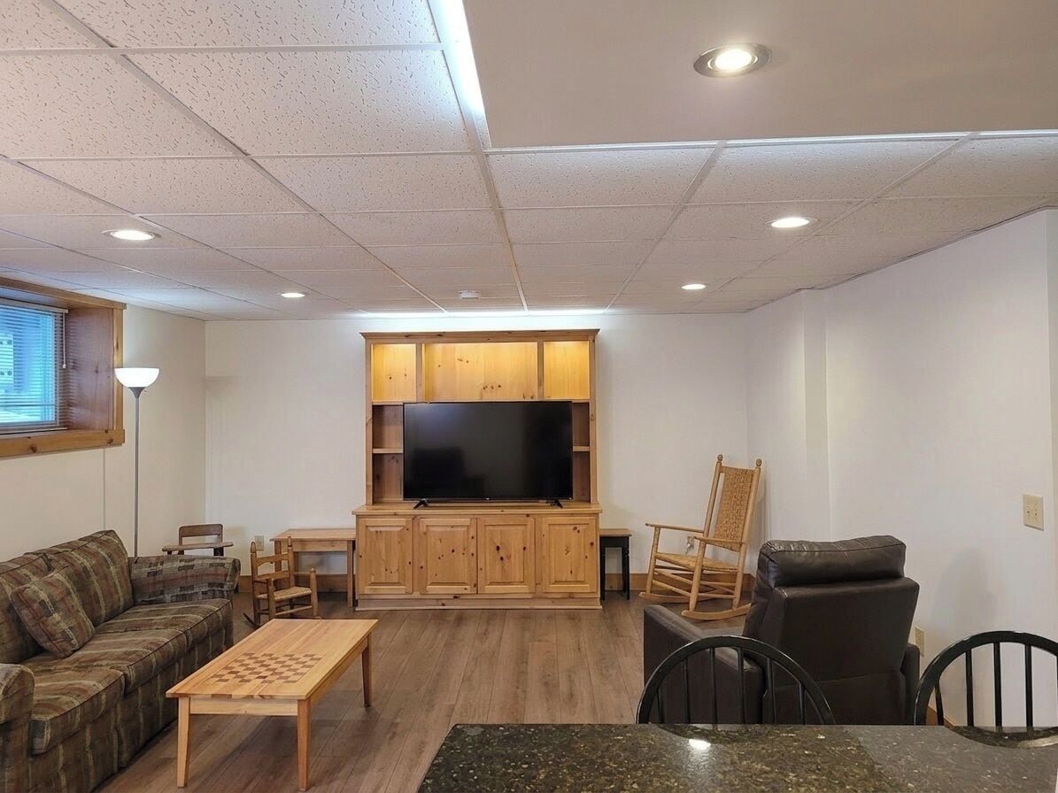 A living room with a flat-screen TV, wooden cabinets, a sofa, a coffee table, and a dining area.