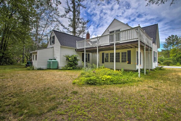 A two-story house with a porch, surrounded by a grassy yard and trees. - Modern Home ~ 2 Mi to Cranmore Mountain Resort! (Conway)