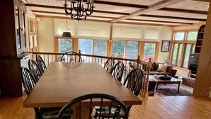 A spacious dining area with a long wooden table and black chairs, a chandelier, and large windows offering a view of the outdoors. - Spacious Villa with Beautiful Views and Great Energy!!! (Stowe)