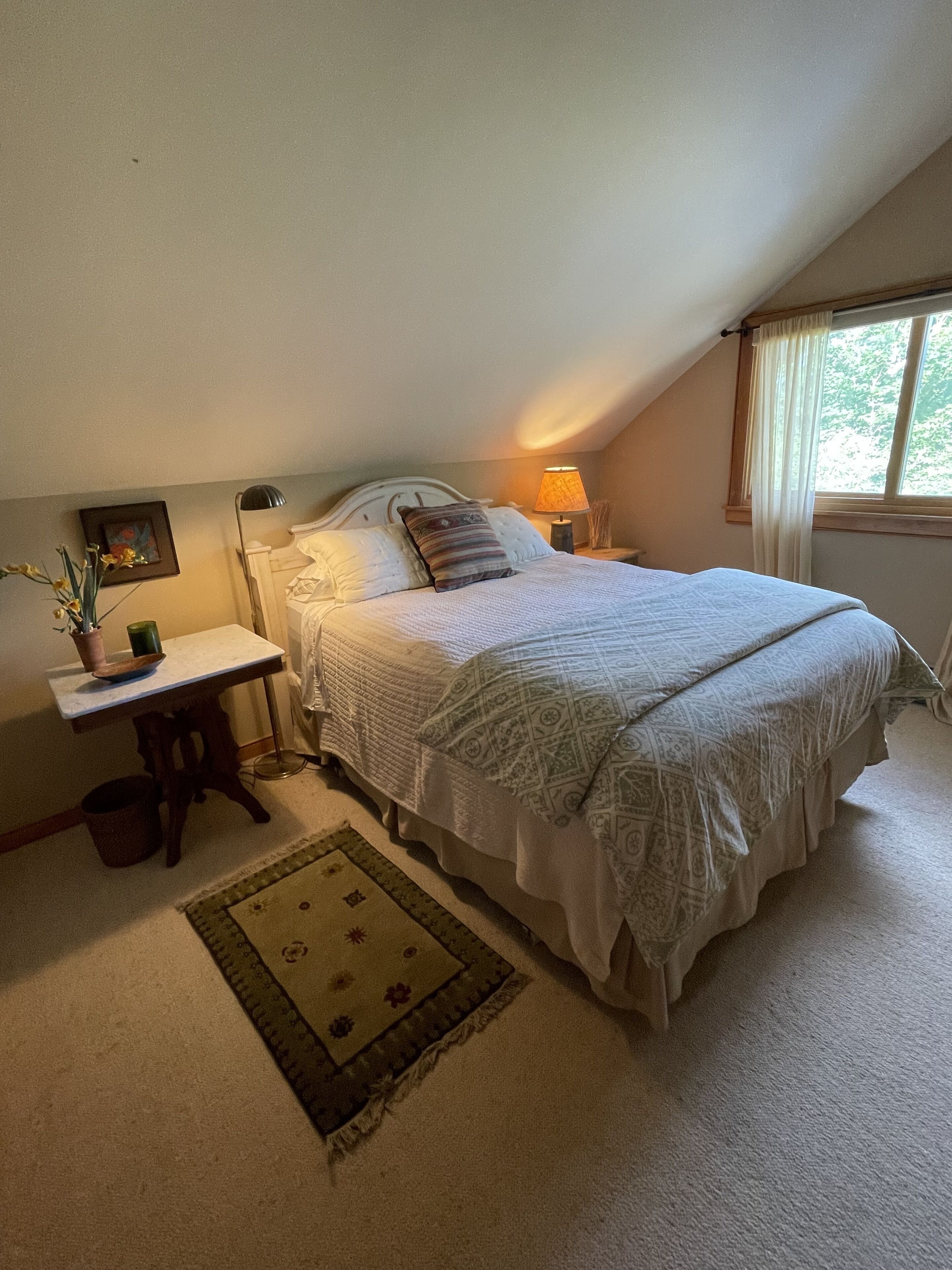 A bedroom with a bed, bedside table, lamp, and a window with curtains.