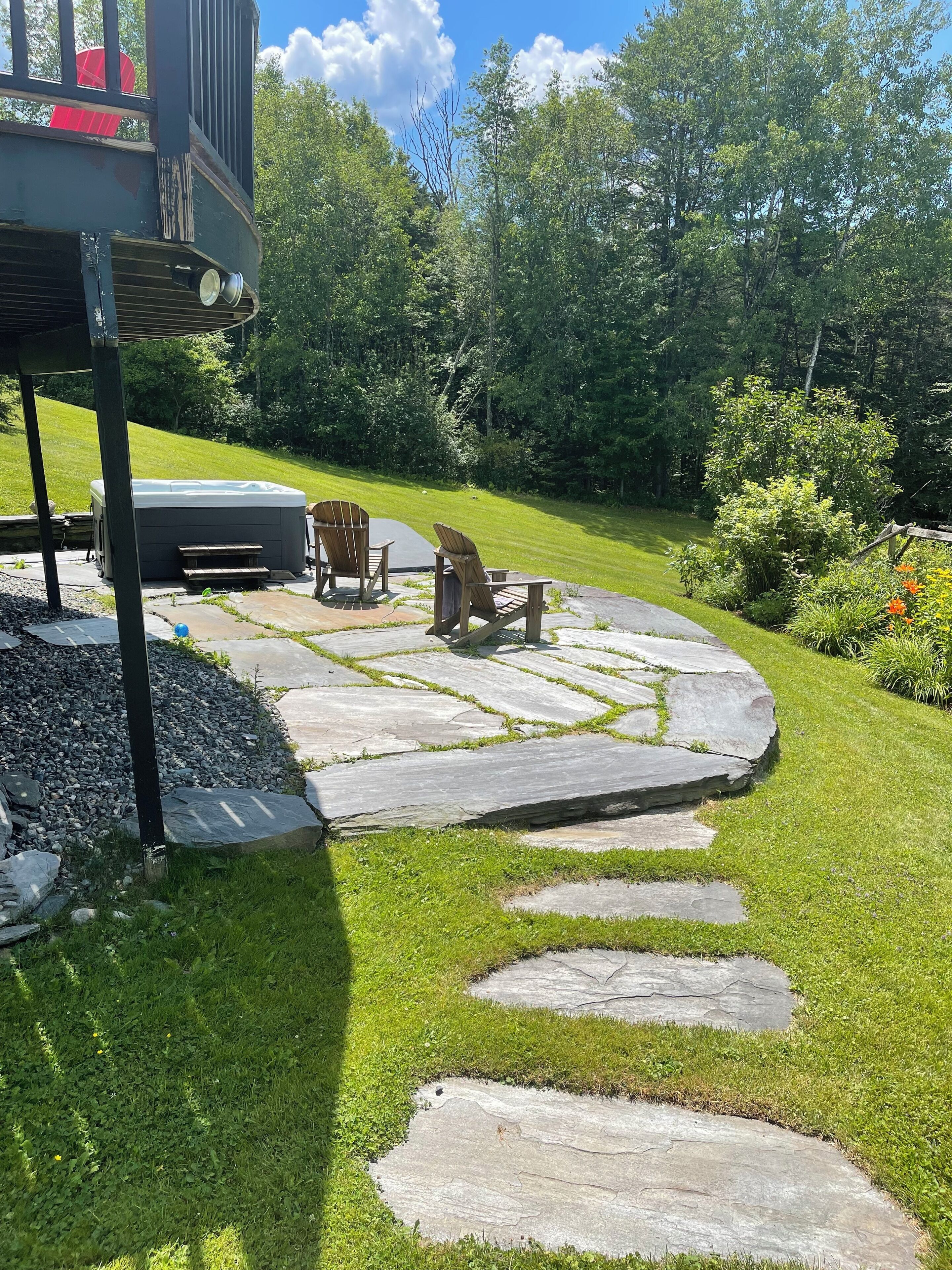 A patio with stone steps, a hot tub, and Adirondack chairs.