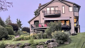 A two-story house with a balcony on the upper floor, surrounded by a well-maintained garden with various plants and a lawn. - Spacious Villa with Beautiful Views and Great Energy!!! (Stowe)