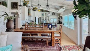 A spacious kitchen with white cabinets, a wooden dining table, and hanging crystal chandeliers.