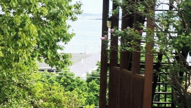 Une pergola en bois offrant une vue sur une étendue d’eau et une côte lointaine.