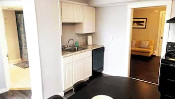 A compact kitchen with white cabinets, a black countertop, and a black dining table with a bowl.