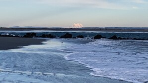 A beach with waves, rocks, and distant icebergs.