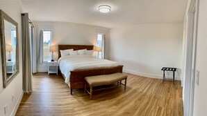 A bedroom with a wooden bed, a bench, a nightstand, a mirror, and a window with curtains.