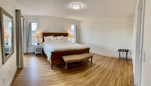 A bedroom with a wooden bed, a bench, a nightstand, a mirror, and a window with curtains.