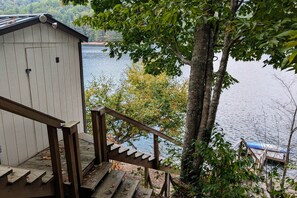 Un escalier en bois mène à une jetée surplombant un lac paisible, le tout étant entouré d’arbres et d’une petite cabane.