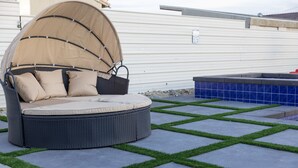 Un área de estar circular al aire libre con toldo, jacuzzi y patio con césped artificial.
